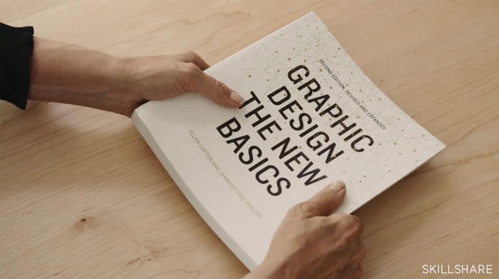 A graphic design book being held by a person over a wooden table