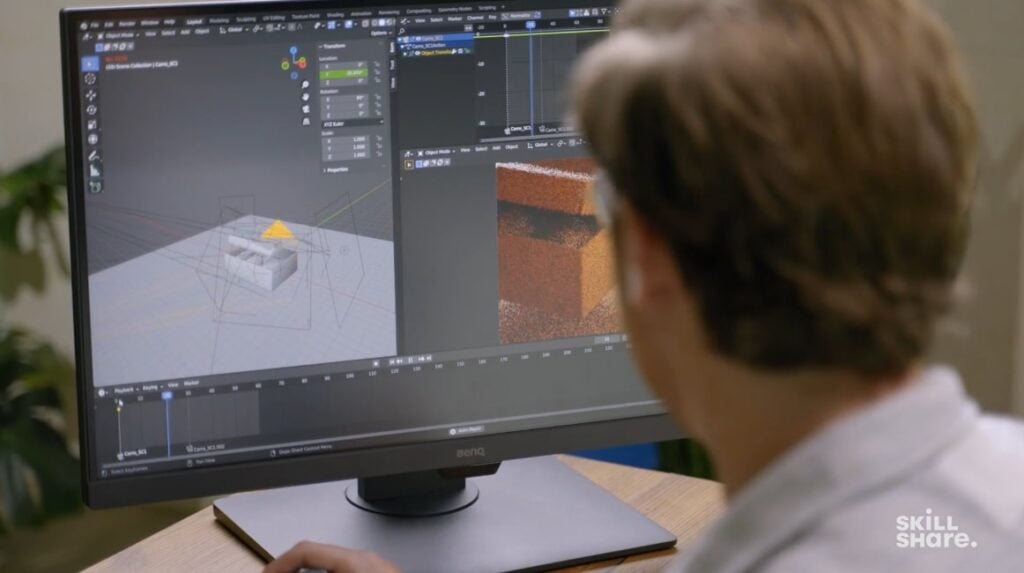 A man sitting at a desk and looking at a computer monitor. The 3D software Blender is open on the monitor, and it displays a work-in-progress animation of a box being opened. 