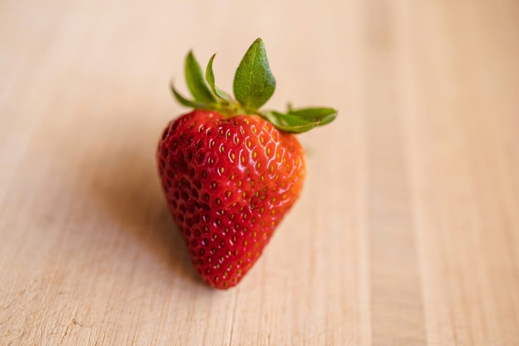 A photo of a single strawberry on a wooden surface.