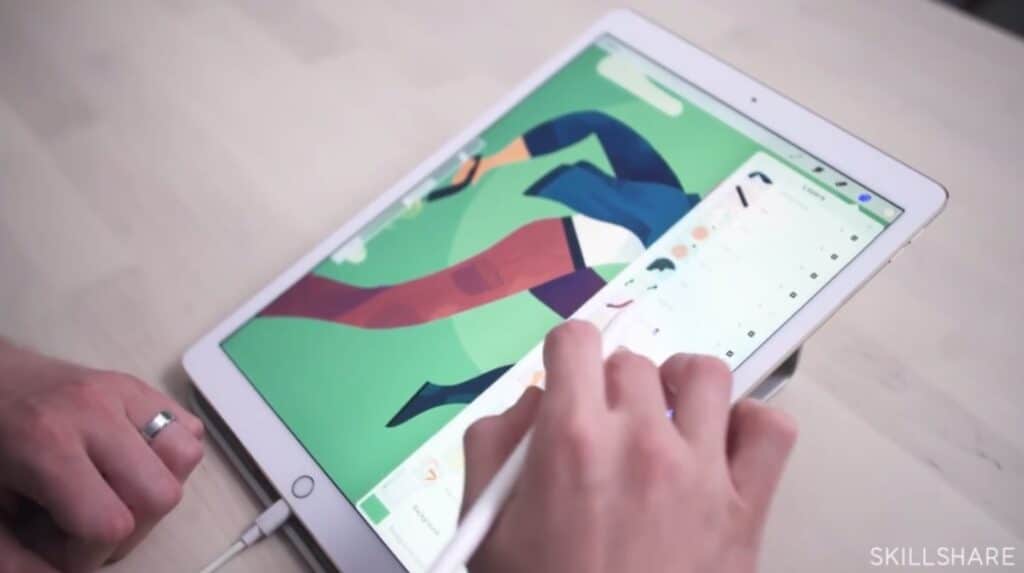 A person’s hand holding an Apple Pencil over an iPad laying on a wooden tabletop. The drawing app Procreate is open on the iPad, and displays a drawing of a person running. The person is using their Apple Pencil to select one of the drawing’s layers from a drop-down menu. 
