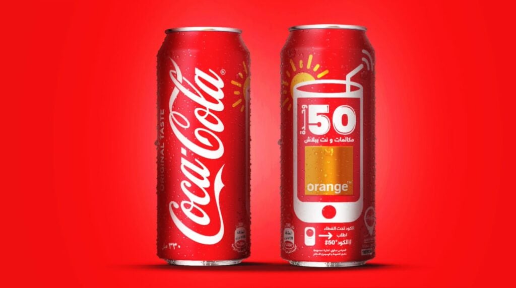 Two images of red Coca-Cola cans against a bright red background. The can on the left shows the classic Coca-Cola logo, while the can on the right contains the words ‘50’ and ‘orange.’