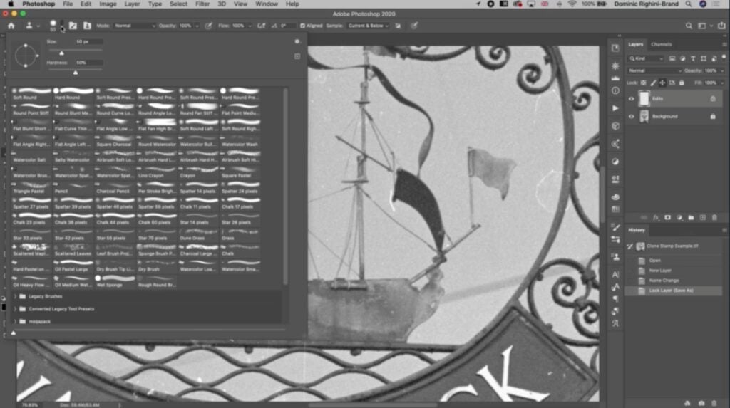 Photoshop is open to a vintage black and white photo of an old, iron sign. The Clone Stamp tool brush settings are open to the left of the screen and over fifty brush types are visible.