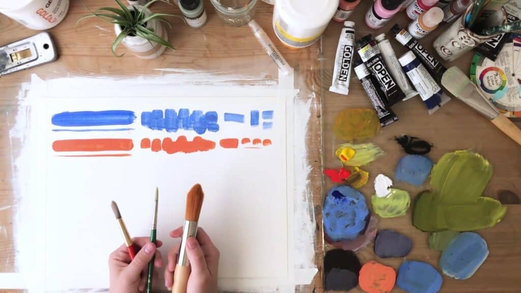 Artist holding three round brushes over their worktable