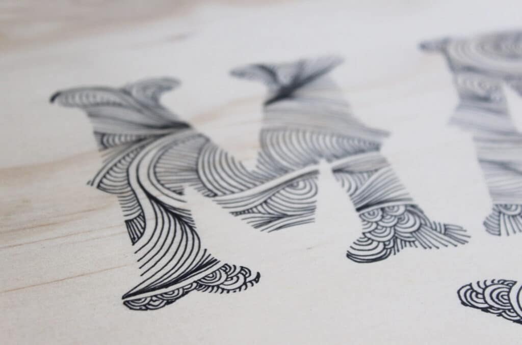 The capital letter M drawn on a wooden surface. The M is composed of concentric waves and arches. 