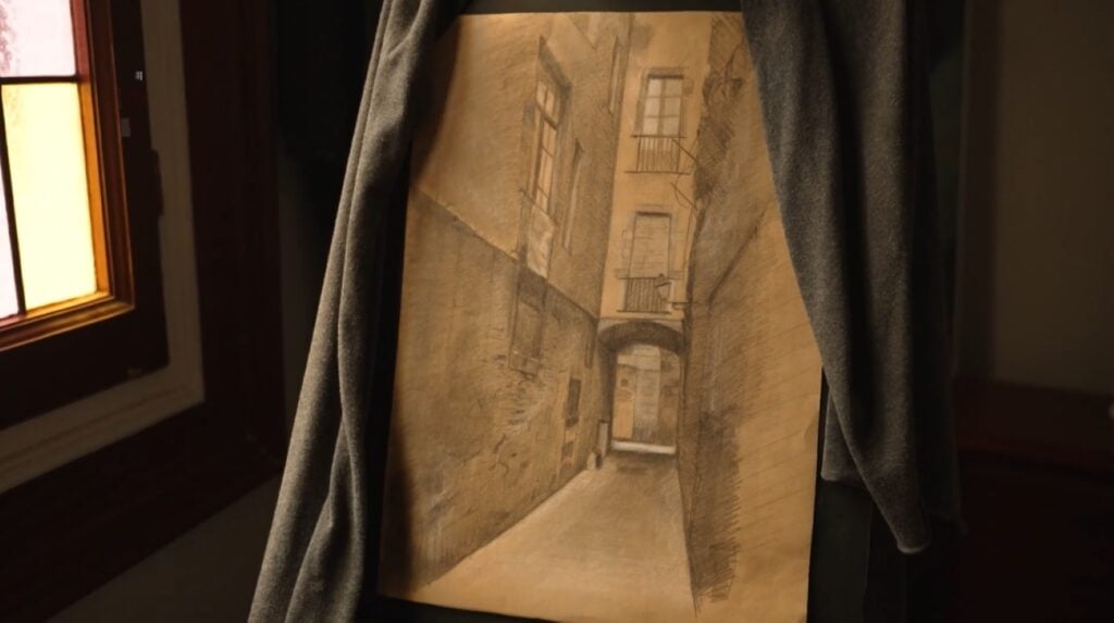 A painting propped up on an easel next to a stained glass window. The painting depicts a sepia-toned alley between two buildings.