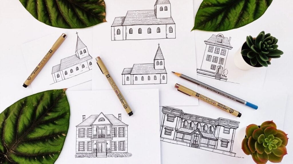 Several pieces of white paper lying on a white tabletop surrounded by plants. Each paper features a pen drawing of a multi-story building.