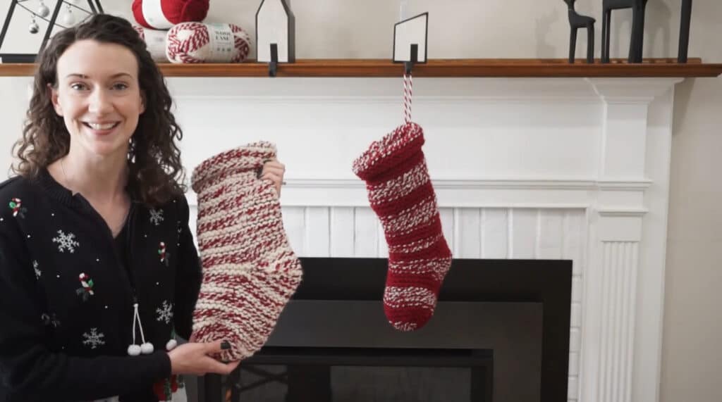 A woman standing in front of a fireplace. There is one red and white knit stocking hanging from the fireplace mantle, and the woman is holding a second stocking in her hands.