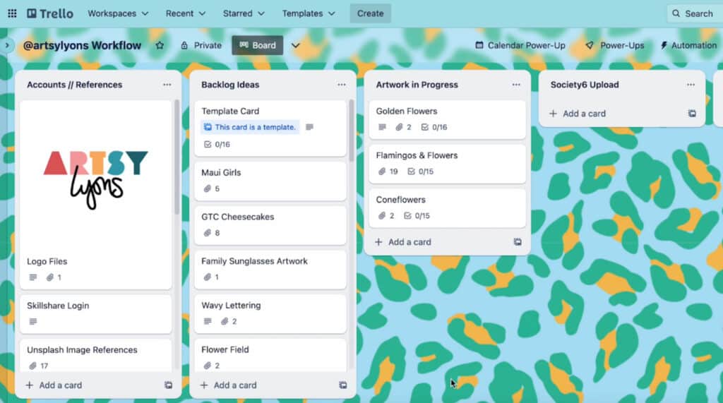 The project management software Trello open on a computer. It’s customized with a green and yellow leopard print background, and shows files organized into four sections titled ‘Accounts/References,’ ‘Backlog Ideas,’ ‘Artwork in Progress’ and ‘Society6 Upload.’