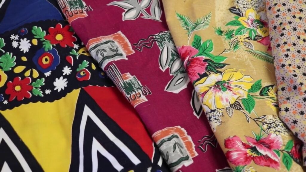 Four different colorful fabrics, one in primary colors and geometric shapes and flowers, one in a rusty orange and wine color, one with pink and yellow flowers on a tan background and one with coral, yellow and dark blue stars and dots on white