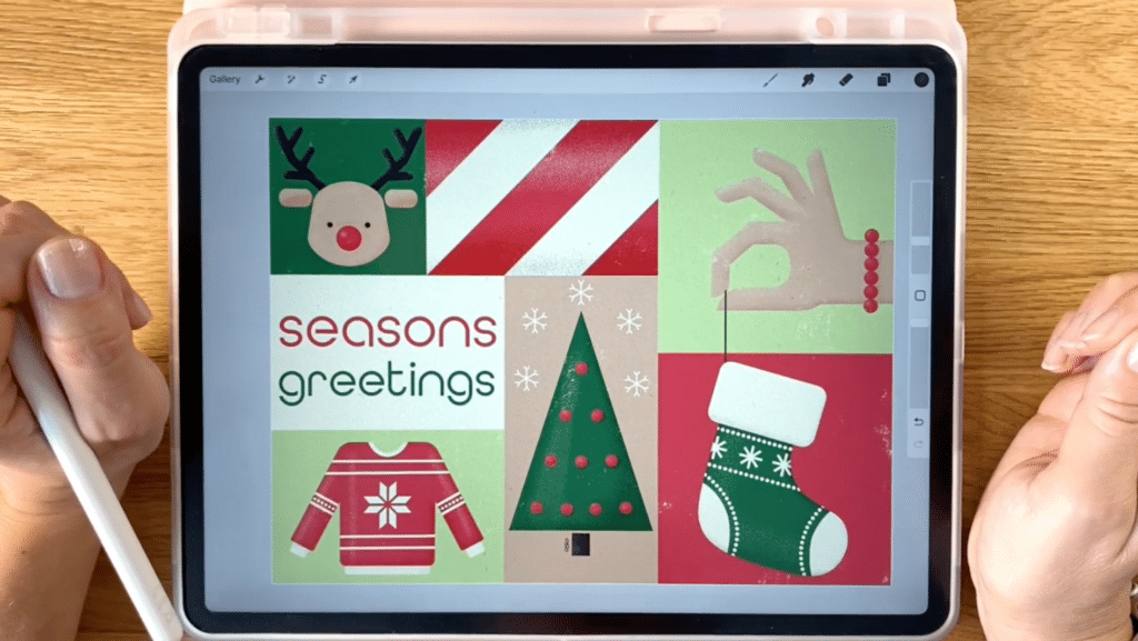 An iPad sits on a wooden table next to two hands. One hand holds an Apple pencil. On the iPad is a holiday illustration that includes a reindeer, a sweater, a Christmas tree and a hand holding a stocking.