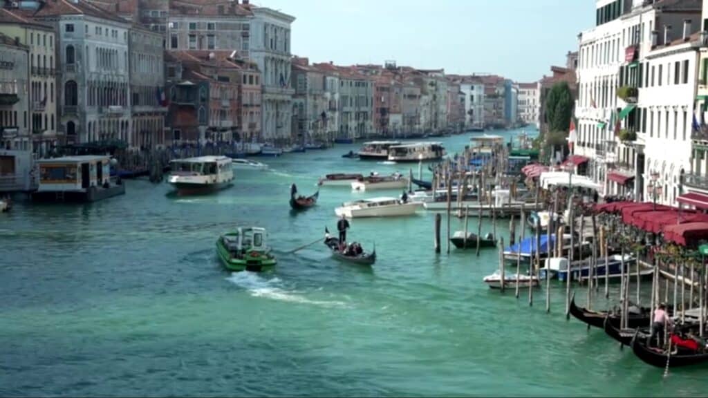 Photo of a European canal full of docked and moving watercraft and flanked by old, windowed buildings