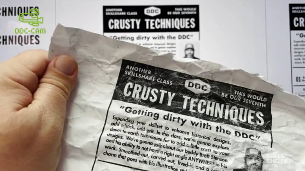 A person’s hand holding a piece of white paper that’s printed with black text. The paper has been crumpled to create creases throughout the text. 