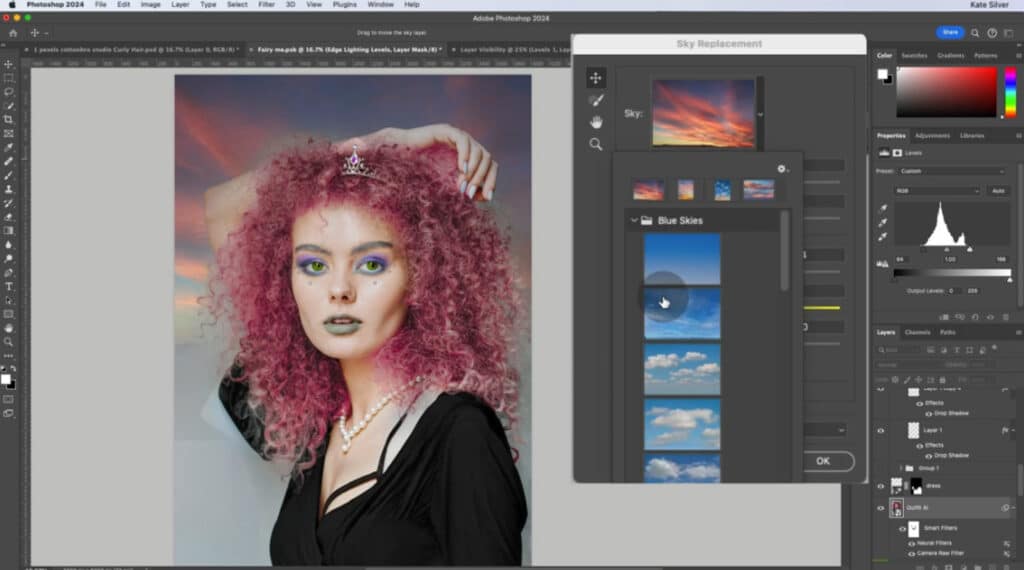 Photoshop open on a computer. The canvas depicts a photo of a woman with pink curly hair. The user is using the software’s Sky Replacement feature to add a pink and blue sunset sky to the photo. 