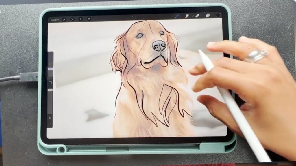 Tablet with screen showing a faded picture of a golden retriever, and an artist’s hand using a stylus to draw over it in black outline
