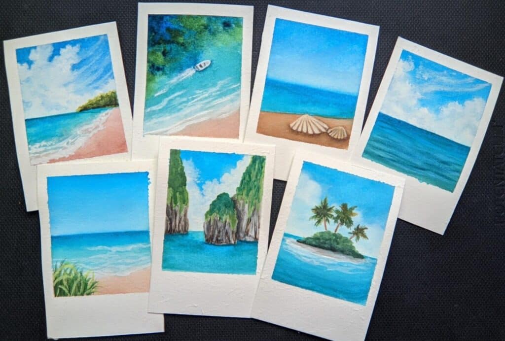 Five small watercolor paintings arranged on a black tabletop. Each one depicts an ocean-themed scene involving bright blue water. They have all been cut out so they resemble the size and shape of Fujifilm Instax Mini instant film.