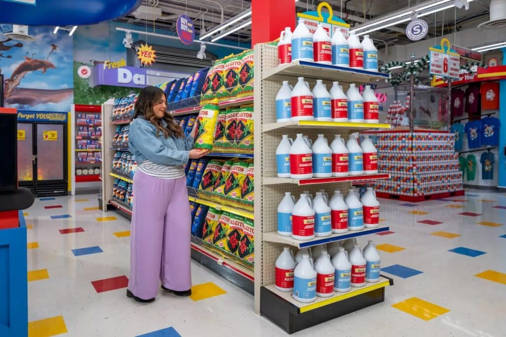 A woman exploring the aisles of Meow Wolf’s grocery-store-like Omega Mart art installation. She’s picking up a bag of chips from a shelf to take a closer look.
