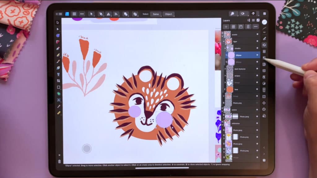 Affinity Designer open on an iPad which is lying on a purple tabletop. A person is using an Apple pencil to draw an illustration of a tiger’s face within the app. 