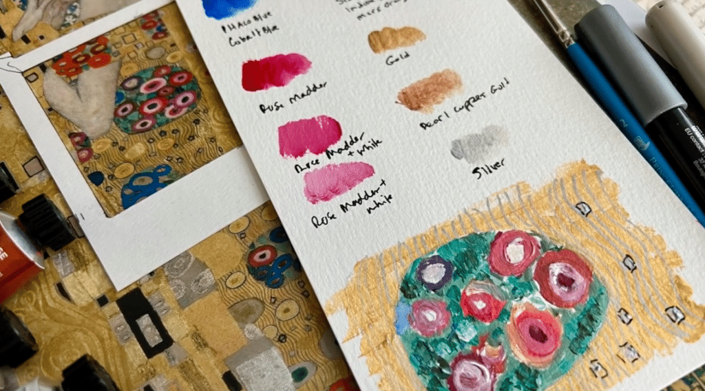 A white piece of paper sits next to multiple images of Gustav Klimt’s work, a few tubes of paint, a marker and a paintbrush. The white piece of paper features multiple paint swatches with each color’s name listed beneath it including gold, silver, rose madder and more. A replica of one of Klimt’s patterns is visible on the bottom of the paper. 