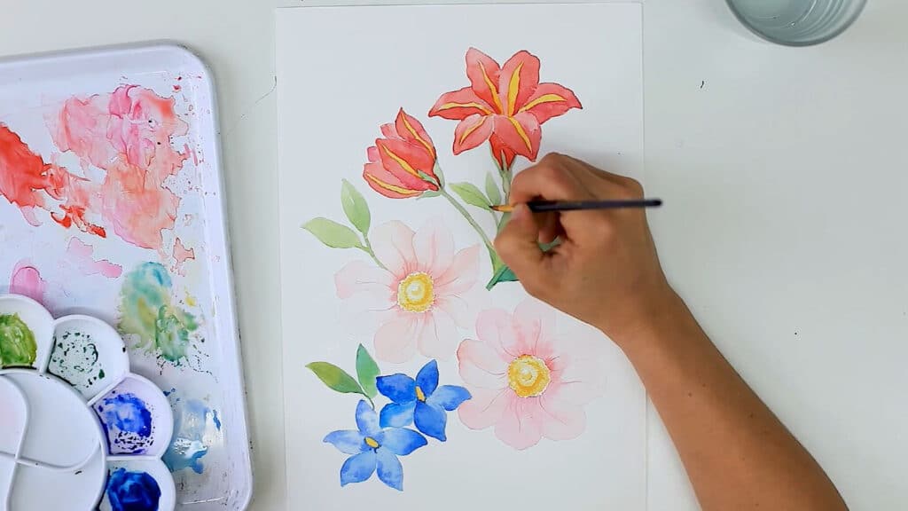 Overhead view of an artist creating a piece of botanical artwork by hand with watercolors and colored pencils