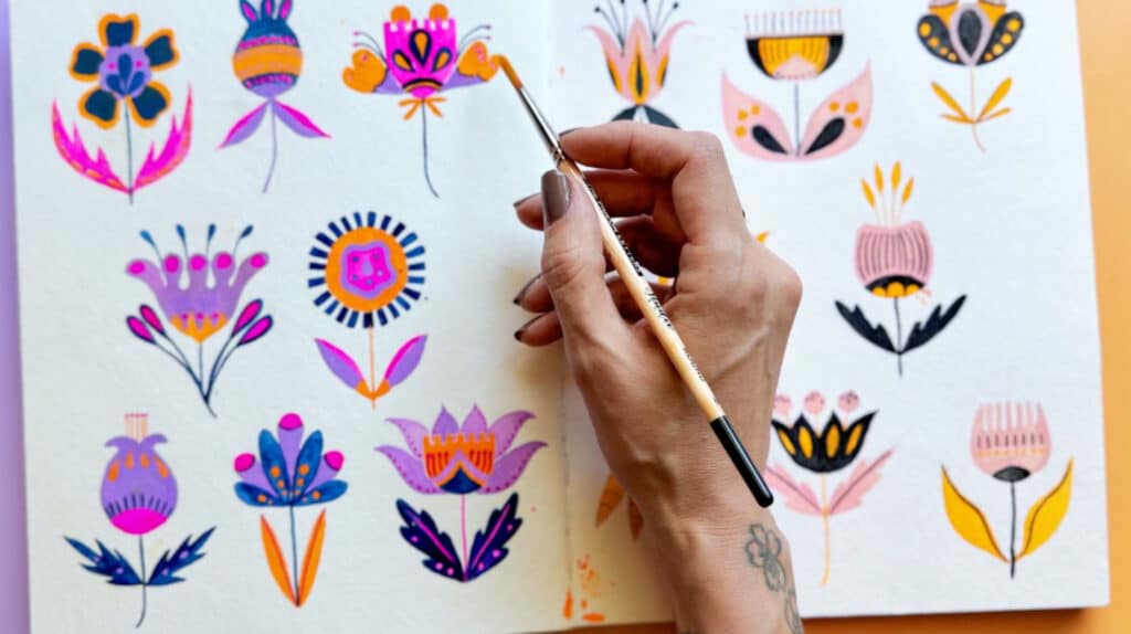A woman’s hand painting stylized, brightly-colored flowers.