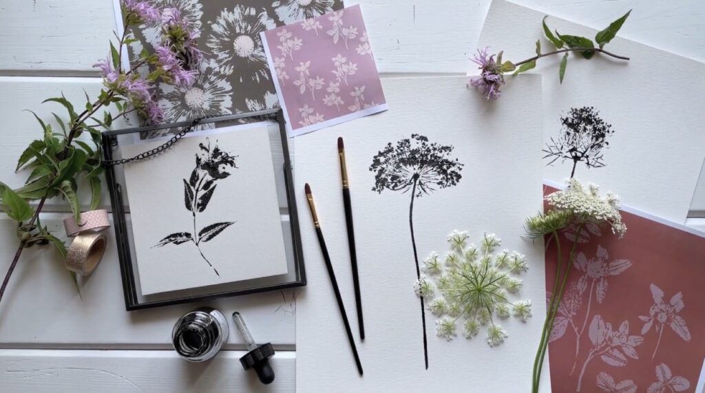 Three botanical prints lying on a white tabletop. All three depict a black ink print of a flower on white paper.