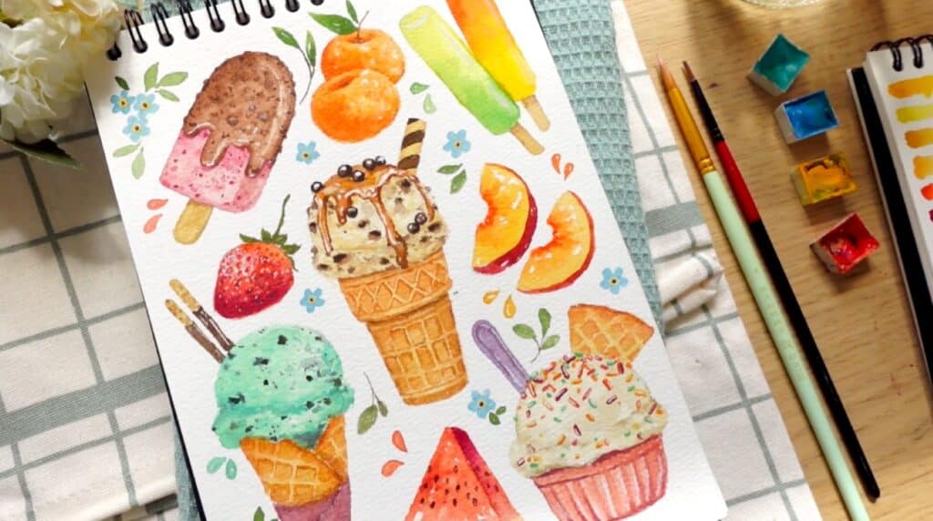 A sketchbook lying open on a wooden tabletop beside paintbrushes and watercolor paint pots. The page is filled with paintings of ice cream, popsicles and various fruits.