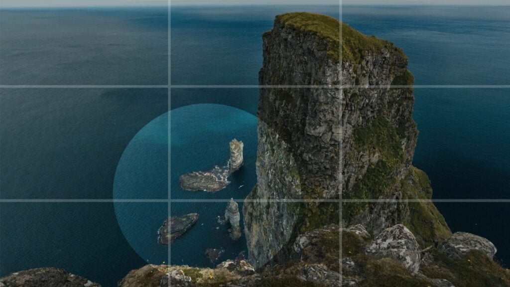A photo of large rock formations in the ocean. The image is overlaid with a 3x3 grid to illustrate proper composition, as well as a ring to highlight the area of focus.