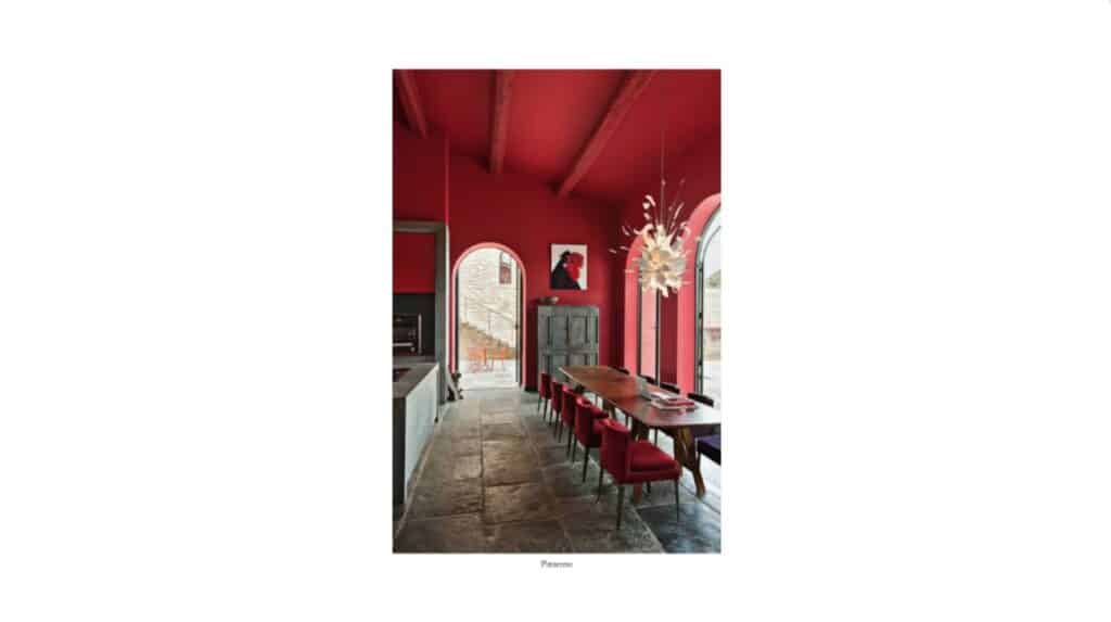 A photo of a dining room with a stone floor and a long wooden table. The chairs around the table are all red, and the ceiling and walls are painted red too. 