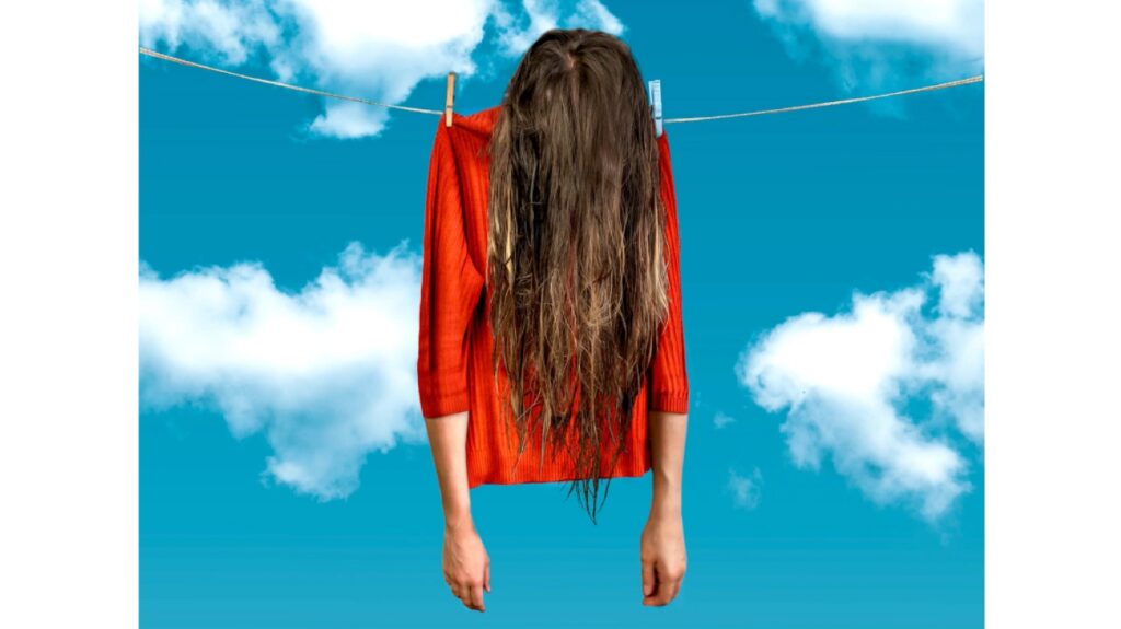 A photo showing a woman in a red sweater pinned to a clothesline like an article of clothing. A blue sky with white clouds is visible in the background.