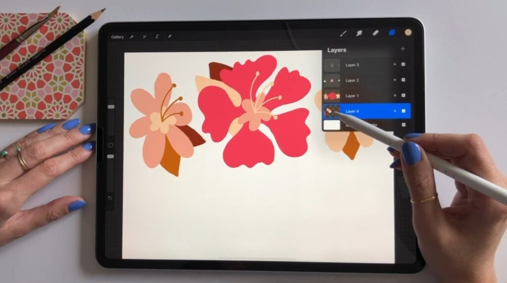 A person’s hand using an Apple Pencil to switch layers within the Procreate iPad app. The app’s canvas shows an orange and bright red floral design.