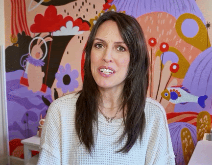 GIF of a brunette woman smiling as she taps her Apple Pencil towards the screen and abstract blobs appear