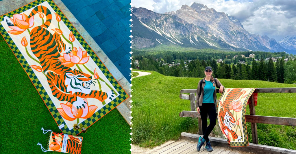 A colorful painting of a tiger next to artist Cat Coquillette holding up this painting in front of a lush mountainscape
